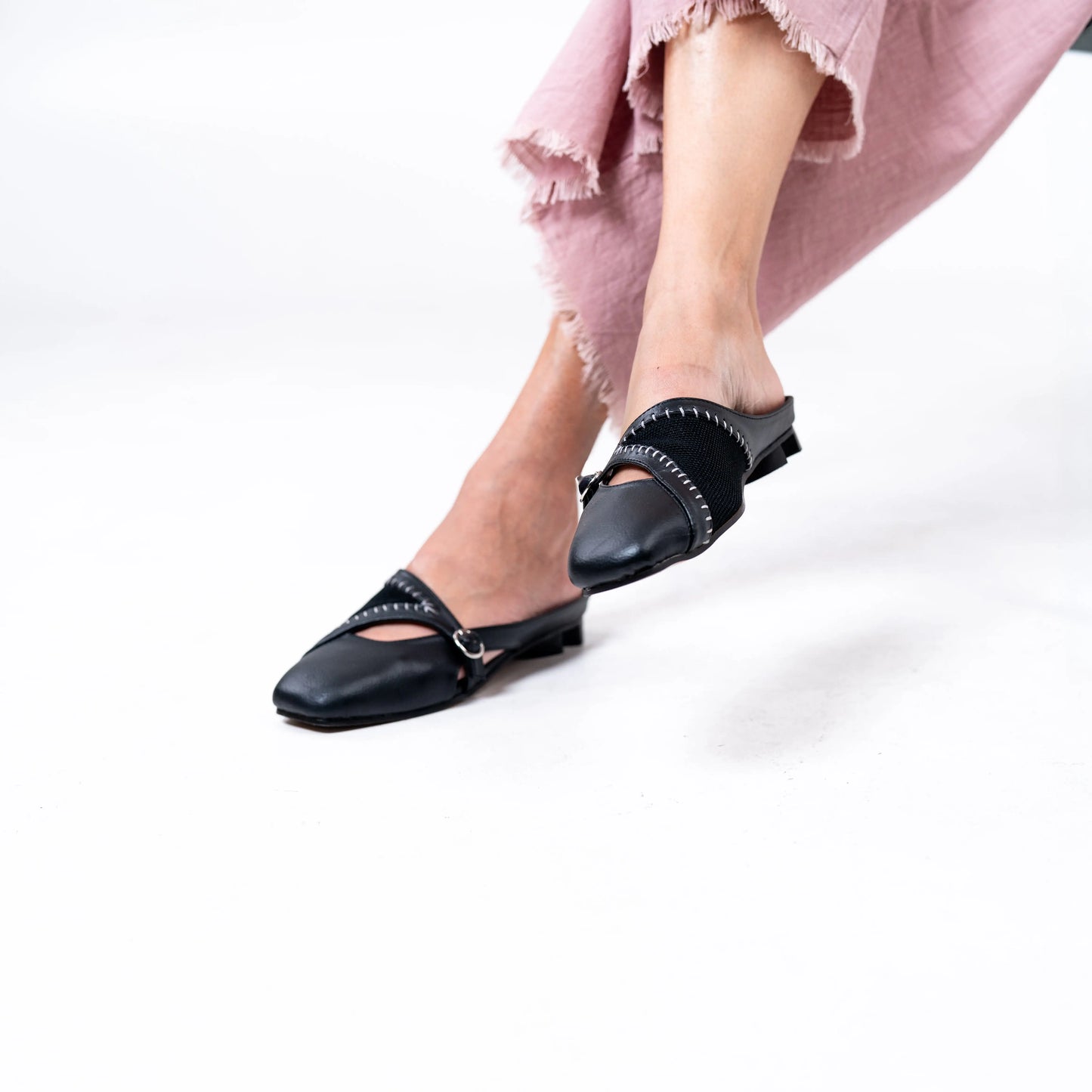 Black flat mules worn with a pink pants on a white background.