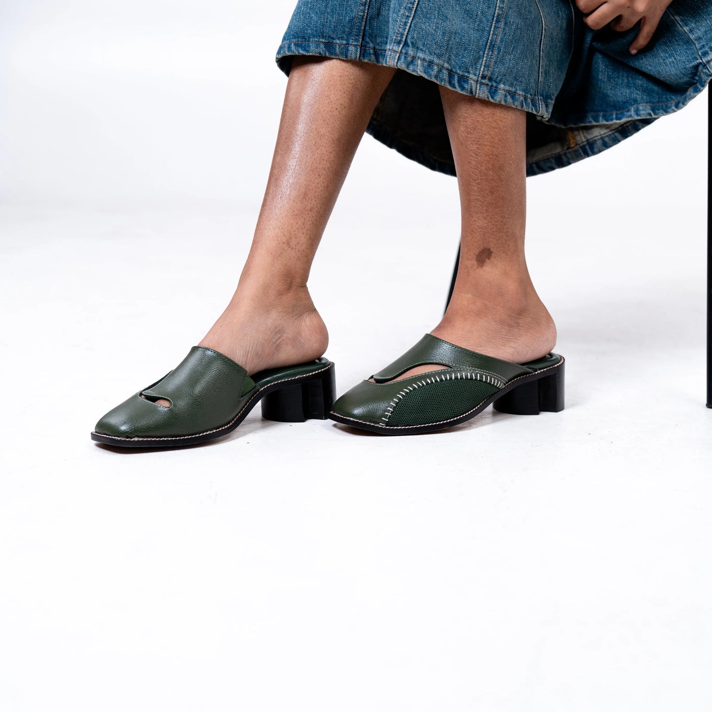 Olive leather shoes worn with a denim skirt on a white background