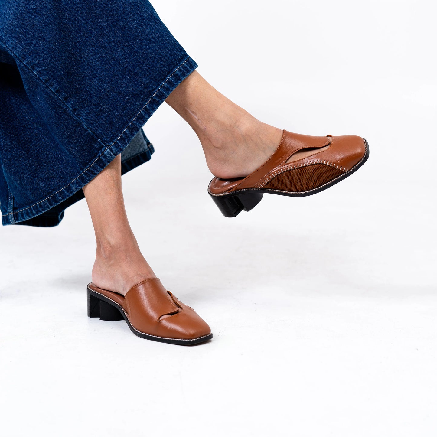 Brown leather shoes worn with blue jeans on a white background