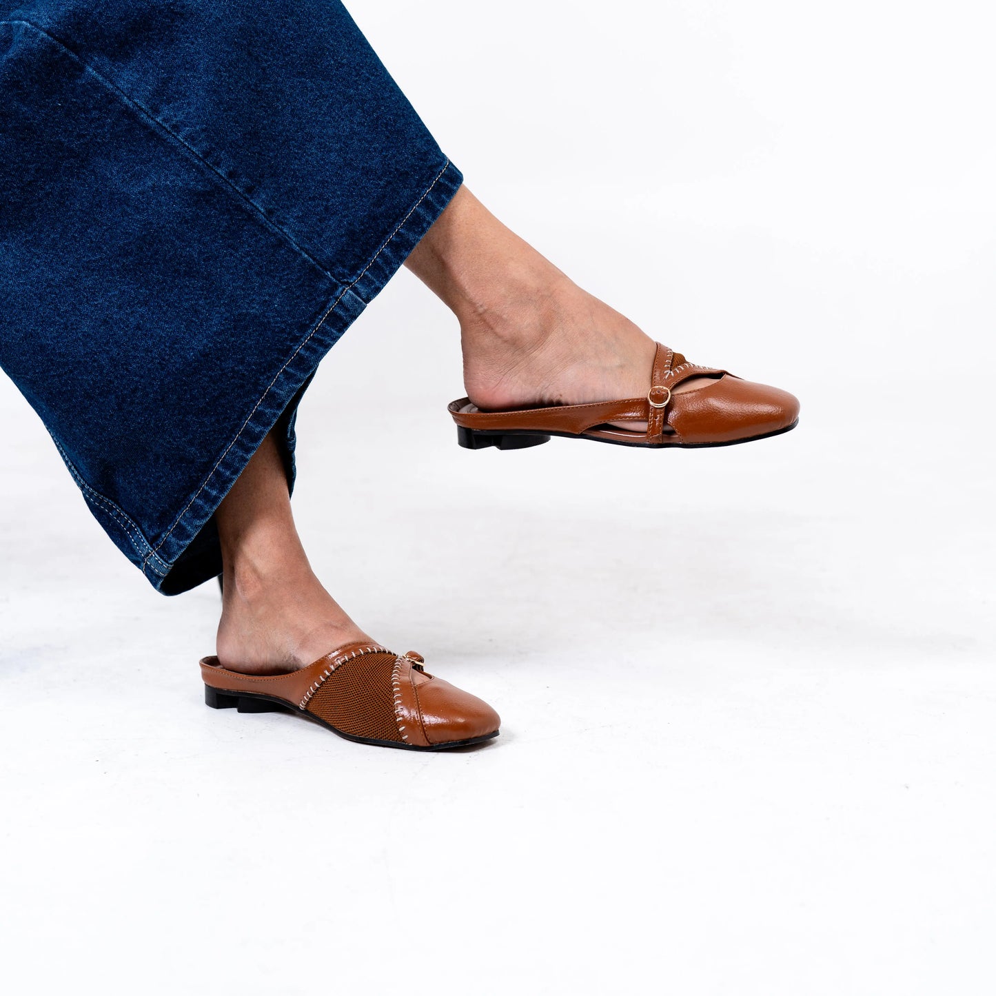 Tan mules worn with blue jeans on a white background.