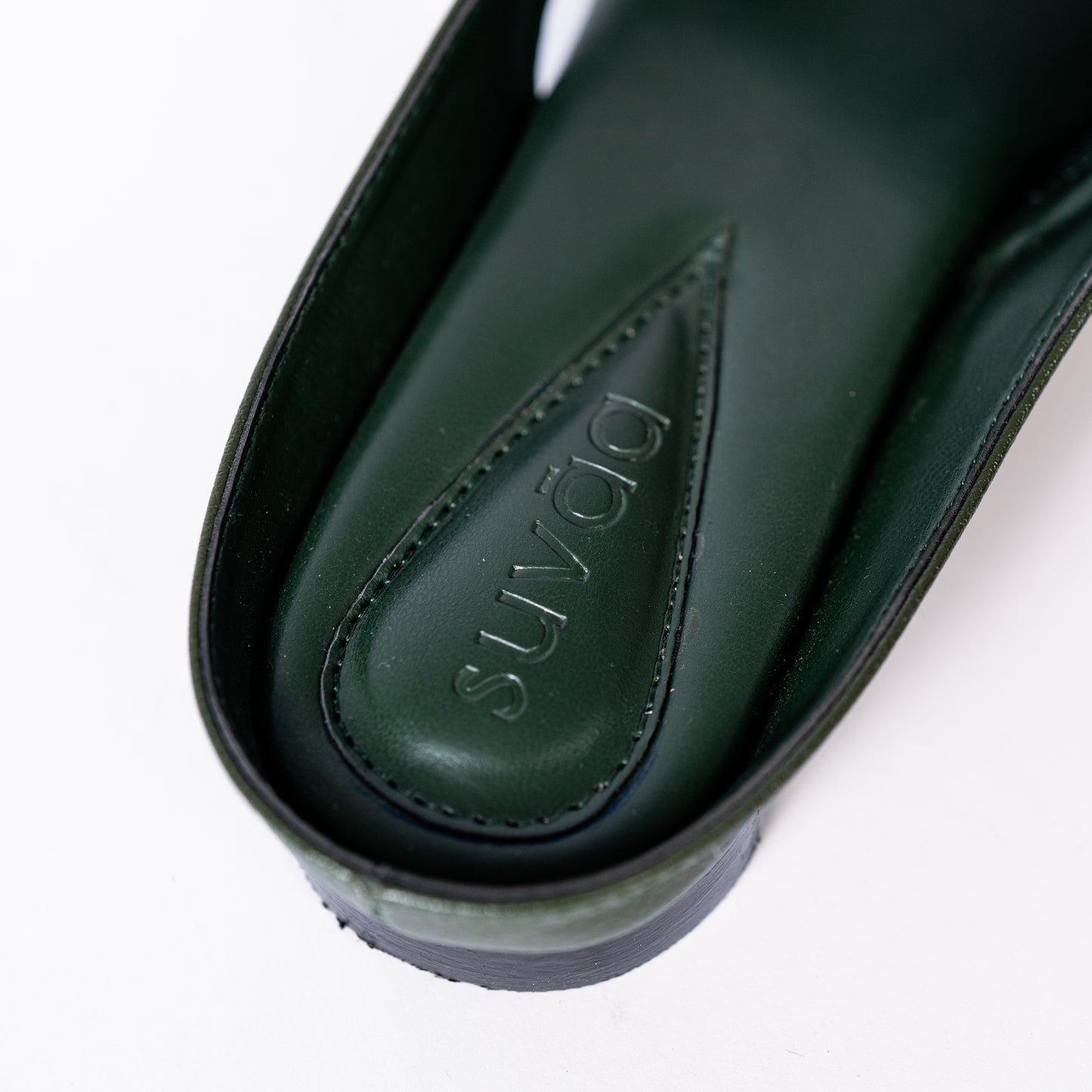 Close-up of a green shoe sole with 'Suvāa' branding on a white background