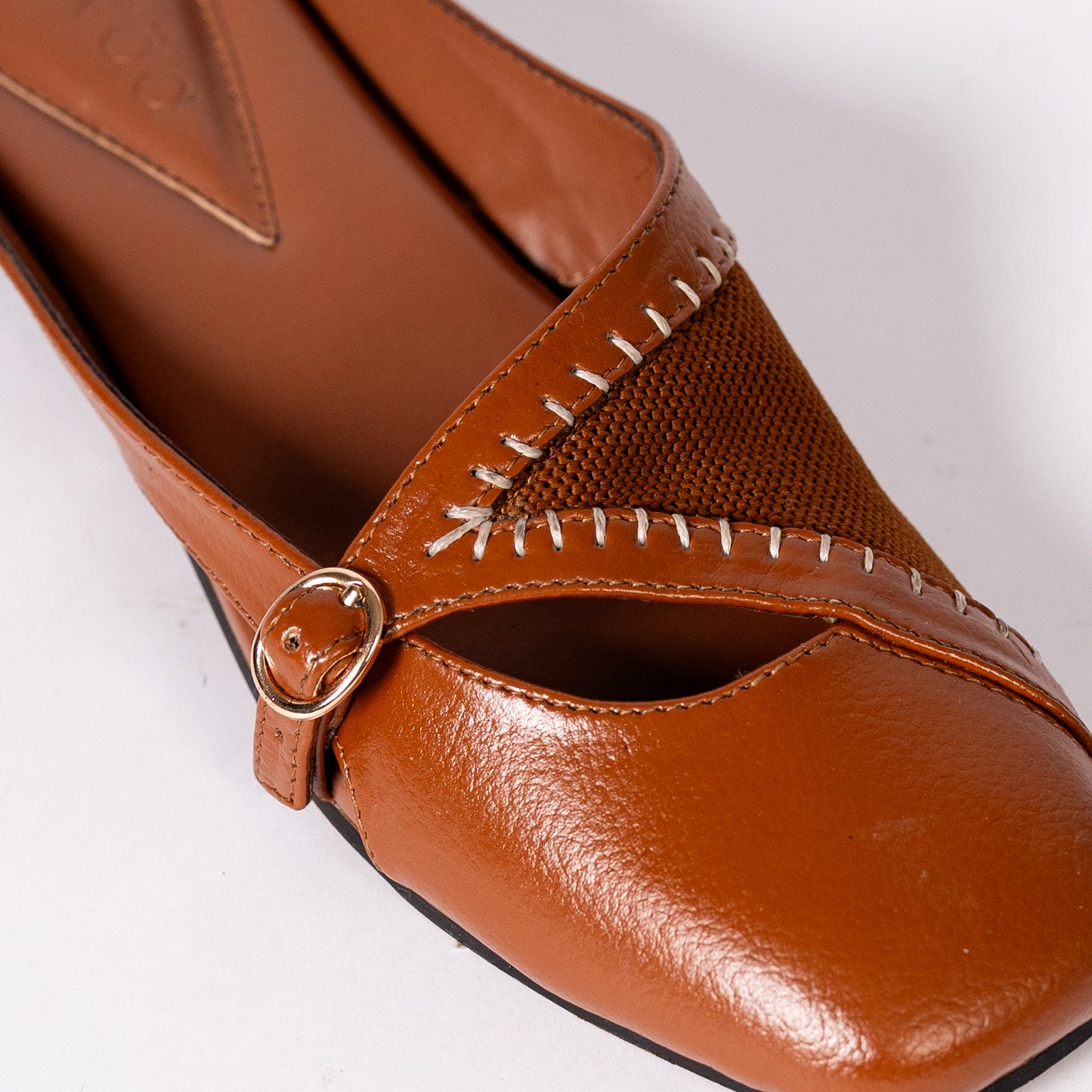 Tan mules with a strap and buckle on a white background.