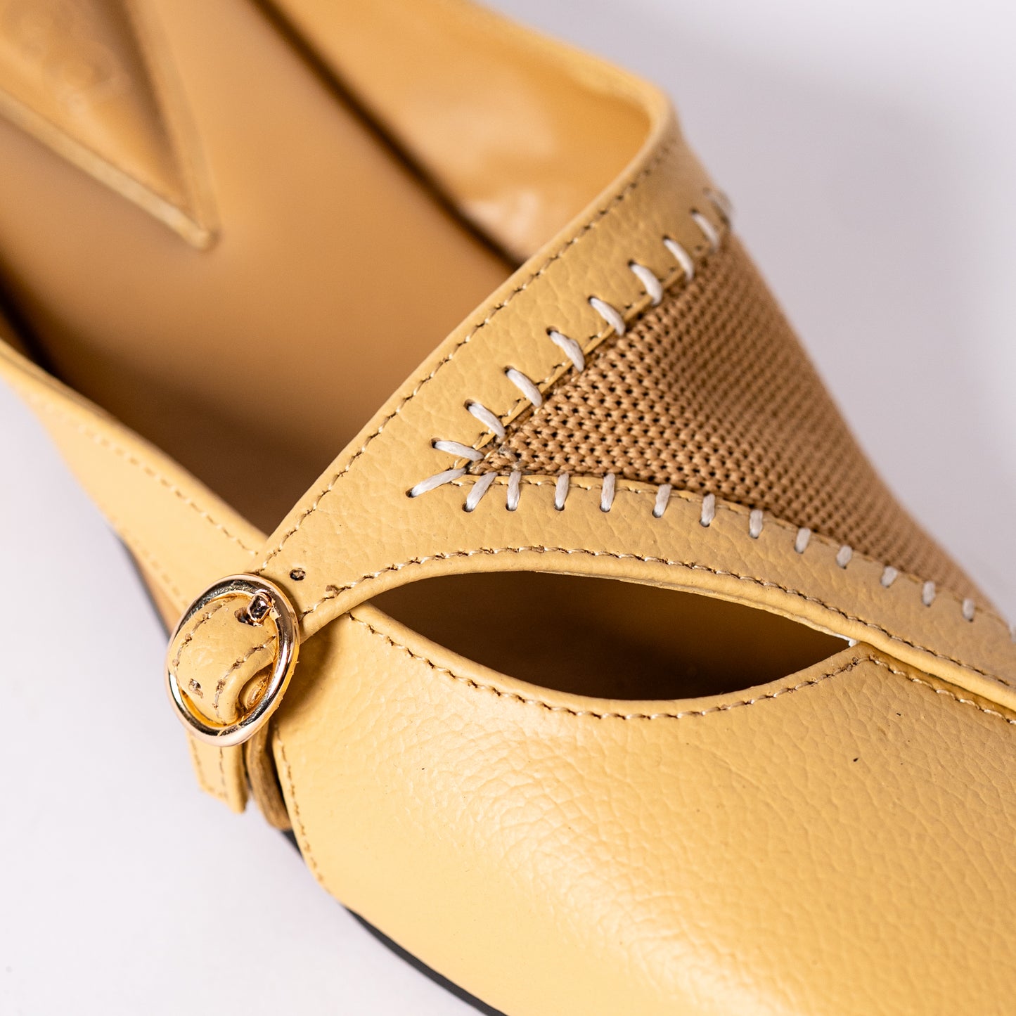 Close-up of a yellow shoe with a strap and buckle on a light grey background.