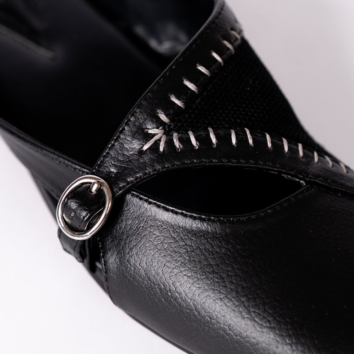 Close-up of a black mule with a decorative buckle on a white background.