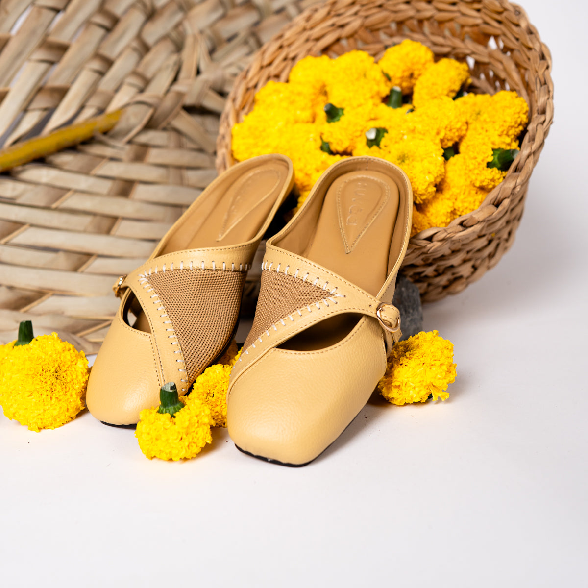 Beige sandals with mesh straps on a white surface with yellow flowers and a woven basket.